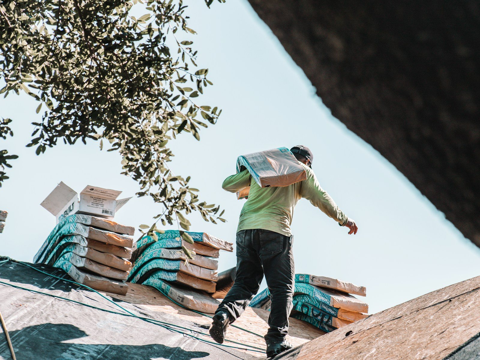 A roofer carrying a bundle of shingles across a residential roofshingle slope