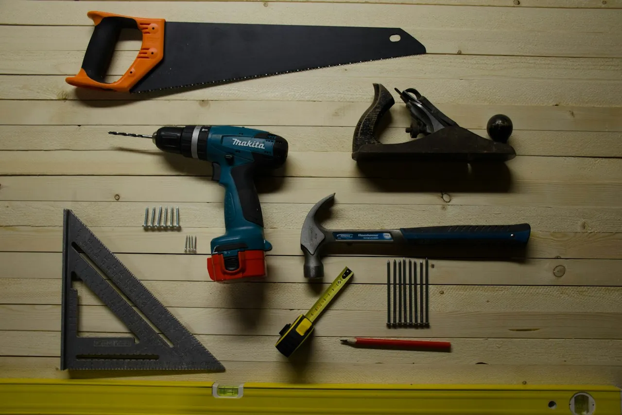 A drill, hammer, saw, square and nails on a wooden workbench